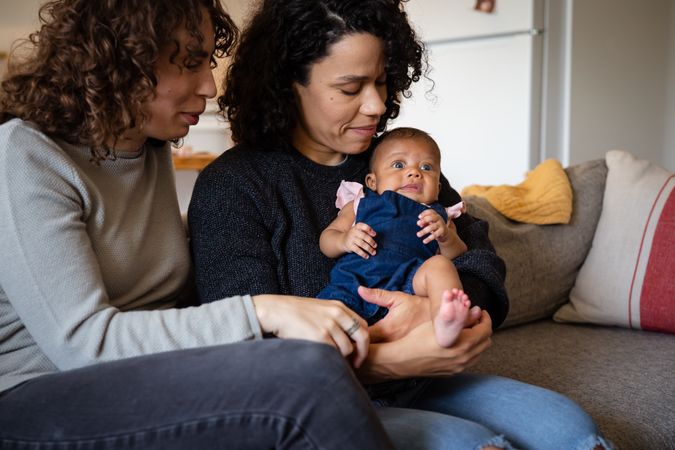 Two new moms on sofa holding their baby