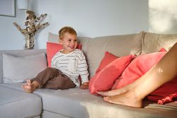 Smiling kid sitting on couch near unrecognizable mother