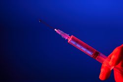 Crop nurse holding syringe with COVID 19 vaccine on blue background