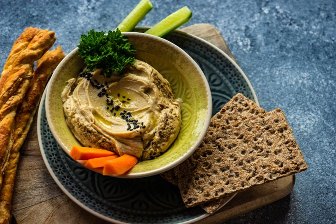 Traditional hummus dish on plate with rye crackers and chopped veggies
