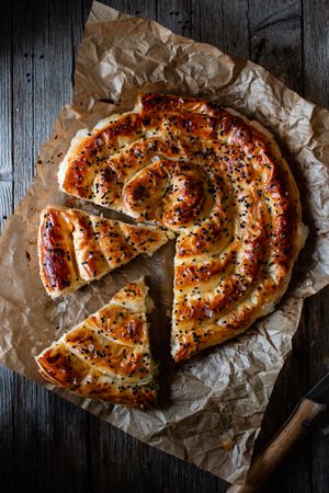 From above crop cook holding hot baking dish with fresh puff pastry and serving piece of borek on plateFaceless person serving homemade borek on wooden table