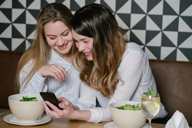 Women friends using smartphone at restaurant table