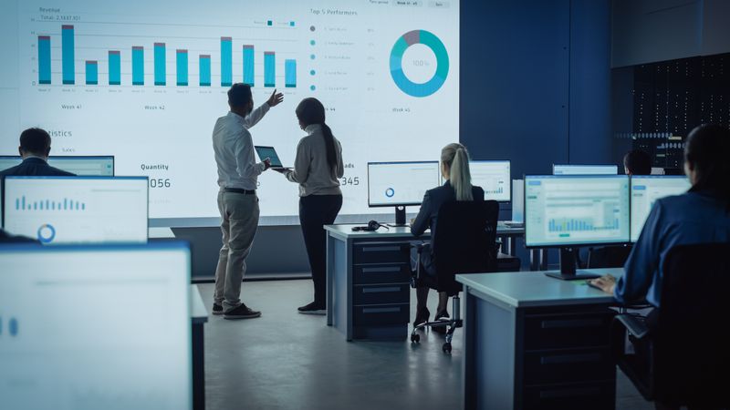 Analysts Review Revenue Data on Large Screen in Modern Office.
