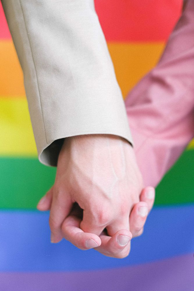 Cropped image of two people holding hands against rainbow flag