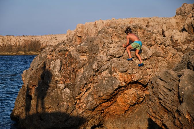 Boy scrambling on stony coast
