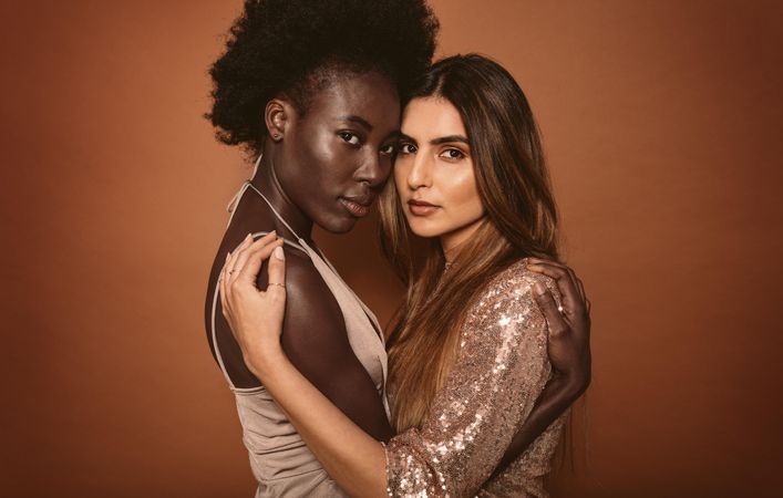 Portrait of two young women embracing on brown background