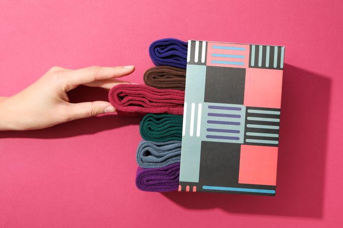 Box with socks and female hand on pink background