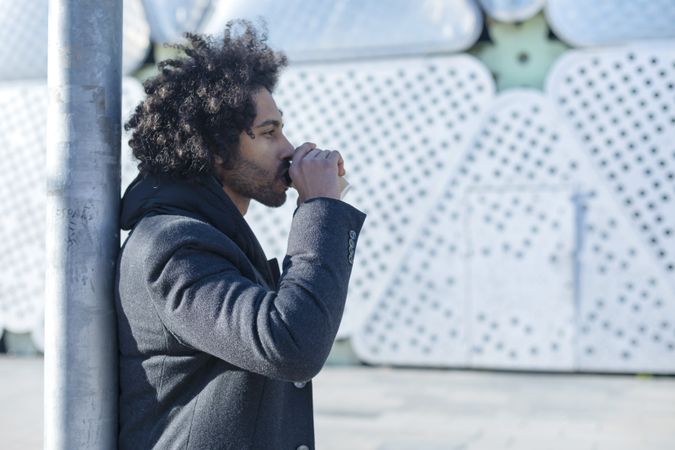 Side view of Black man in jacket sipping warm beverage standing outside