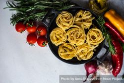 Top view of raw Fettuccine pasta in pan surrounded by fresh vegetables 4jVrmx
