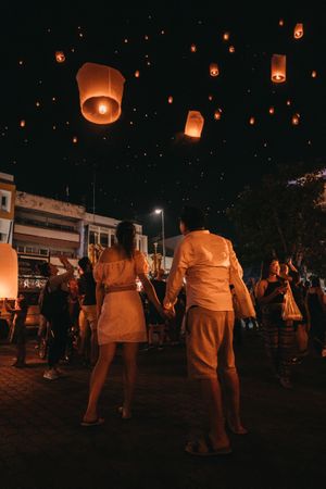 A couple holds hands as they watch lanterns float into the sky