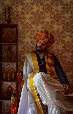 Man wearing turban and light outfit sitting on chair looking away