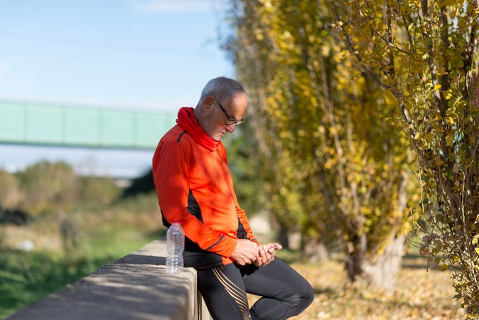 Older male checking phone sitting on divide with water bottle