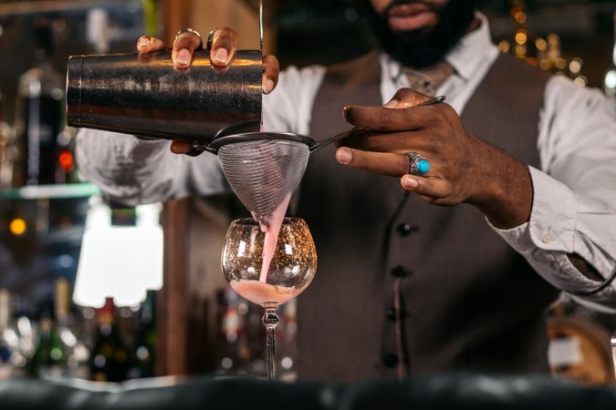 Close-up of the hands of a stylish Black bartender preparing a cocktail in a shaker in a traditional cocktail bar