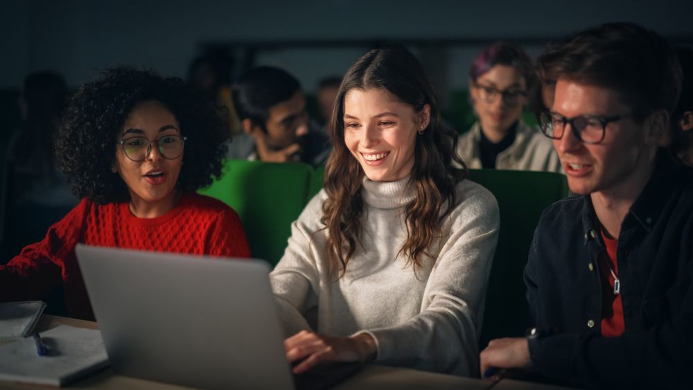 Team of Enthusiastic Students Collaborate in University Classroom, Compare Research Project Work on a Laptop Computer.