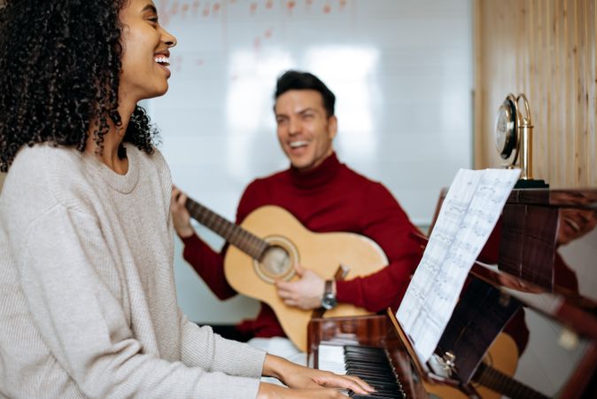 Woman playing piano near man playing guitar in studio