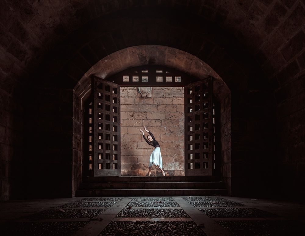 Graceful ballerina dancing in dark passage near stone brick