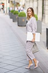 Happy woman in grey walking outside with laptop
