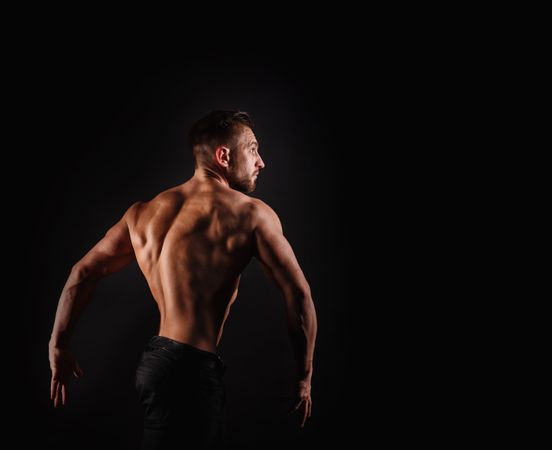 Bodybuilder practicing poses ahead of competition in dark studio, copy space