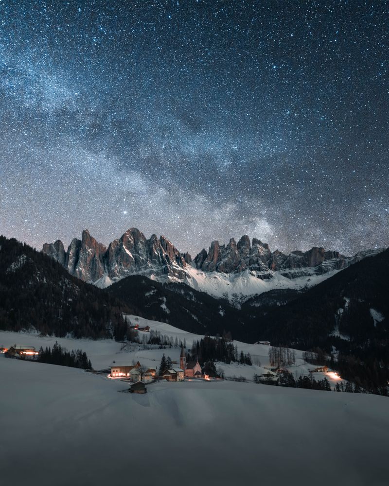Mountain-side houses on snow covered ground under starry night