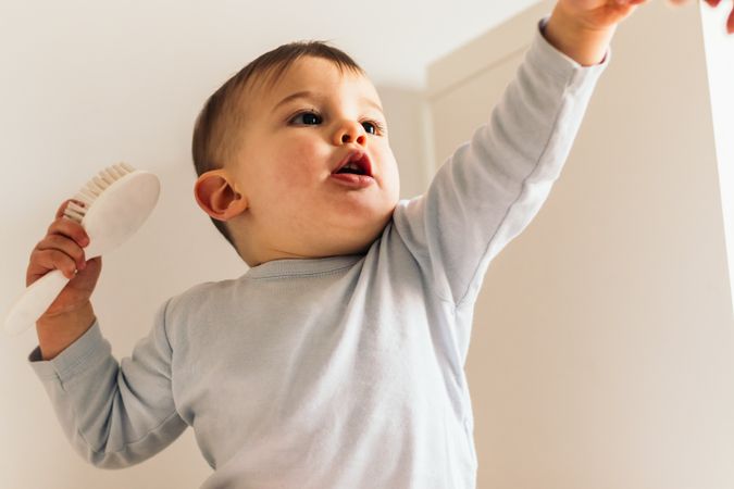 adorable and beautiful baby sitting with a hair brush pointing at something
