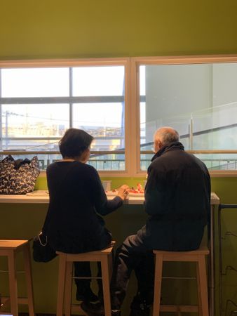 Back view of man and woman sitting on stool chairs eating lunch