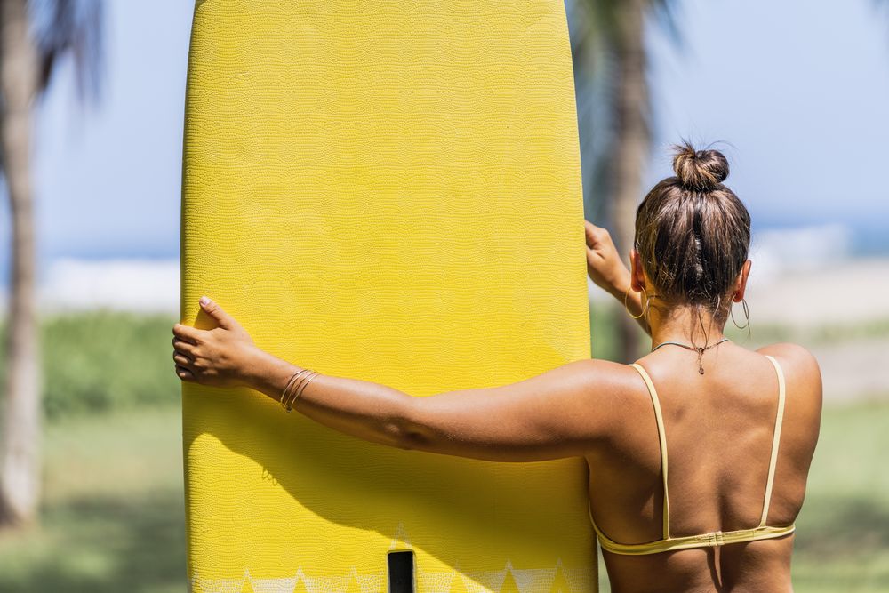 Woman in bikini by bright paddleboard on beach