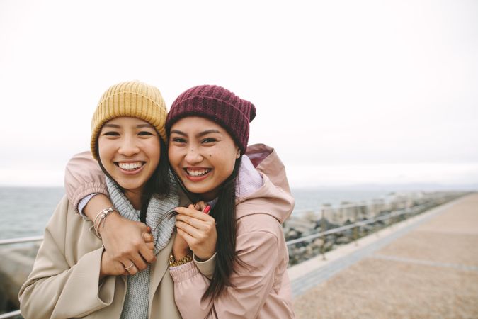 Two happy young Asian women in beanies embracing