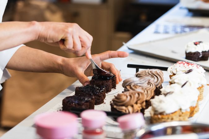 Crop cook smearing chocolate on sponge cakes in bakehouse