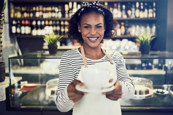 Smiling woman presenting a cup of coffee in bistro