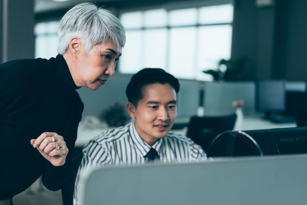 Older Asian woman looking over her male colleagues her