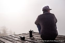 Man in sweater sitting on wooden dock beside coffee pot 5p6V8b