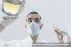 Dentist wearing surgical mask while holding angled mirror and drill, ready to begin work 5qmQK5