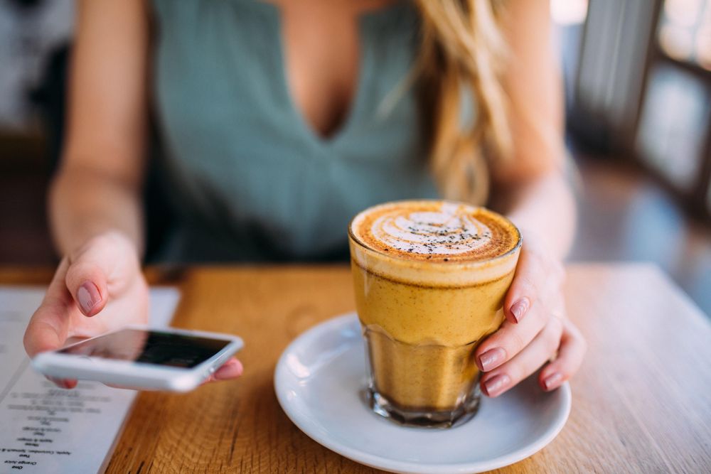 Young woman holding a mobile device and resting a hand on her beverage