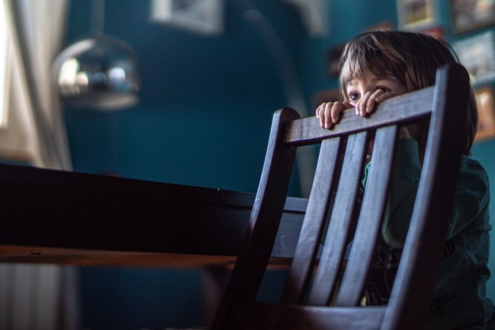 Boy standing behind wooden chair
