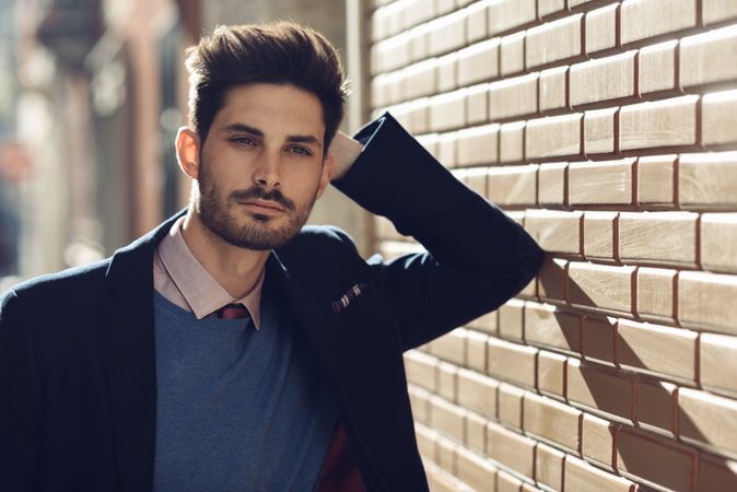 Man leaning on brick wall outside wearing elegant suit, copy space