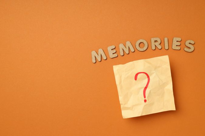 The word “Memories” written in cork on dusty orange background with post it note, copy space