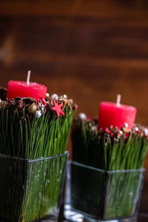 Side view of red Christmas candles with cinnamon and star anise in vase on wooden table