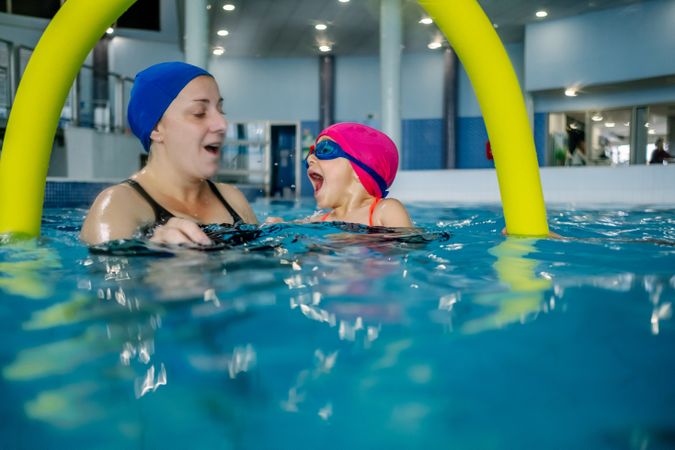 Cheerful girl swimming in pool with mother