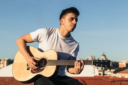 young man sitting playing acoustic guitar on a rooftop