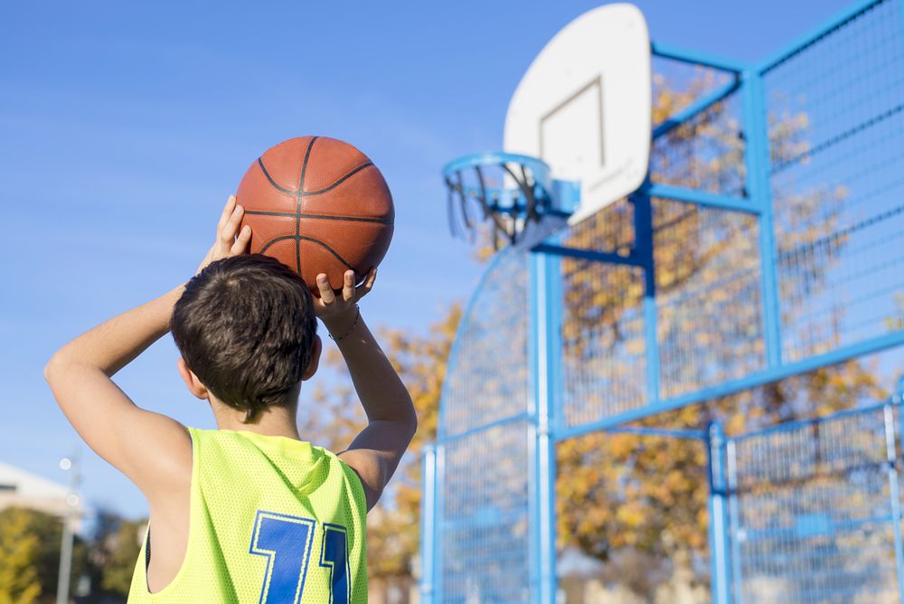 Teenager throwing a basketball into the hoop from behind