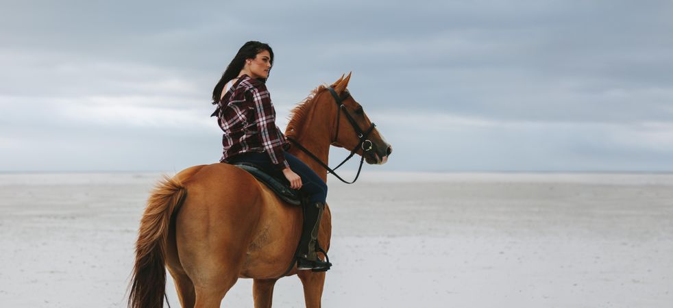 Woman horse riding at the sea shore and looking away