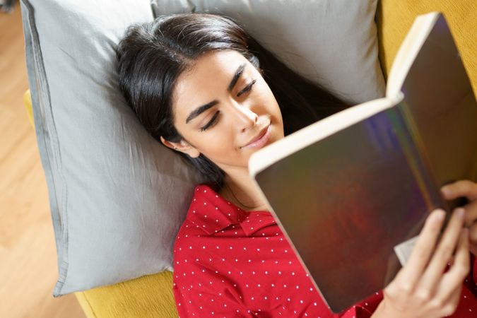 Woman lying on pillows reading a green book