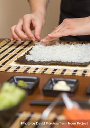 Hands of woman chef preparing sushi rolls with rice on a nori seaweed sheet, vertical 0yWAR4