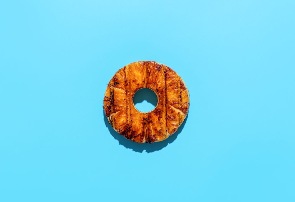 Pineapple slice grilled and topped with rum sauce, minimalist on a blue background