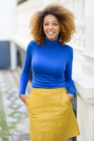 Smiling female with curly hair and boots wearing bright clothes pictured outside