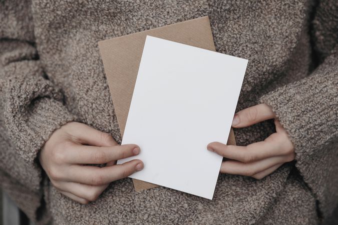 Winter, autumn cozy stationery still life with female hands in beige pullover holding blank greeting card