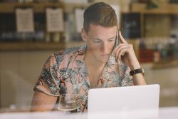 Man talking on smartphone while browsing laptop