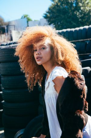 Young woman outside at tire yard with natural curly hair looking at camera