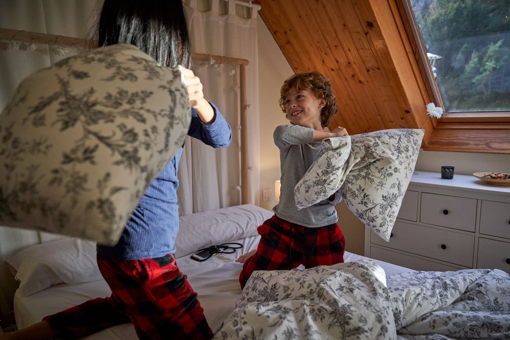 Mother and little son fighting with soft pillows on bed
