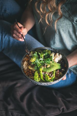 Woman in t-shirt and jeans sitting with fork in vegetarian bowl, vertical composition